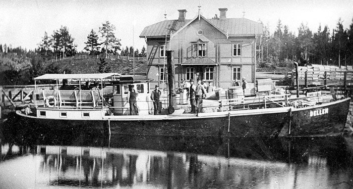 Dellen är ett mindre före detta ångfartyg med öppet däck i fören, midskepps syns en liten styrhytt med skorsten, i aktern en upphöjning vars tak bildar sittplats med ett kapell som solskydd. Ombord syns en handfull människor.  I bakgrunden på det svartvita fotografiet syns bebyggelse och några träd. 