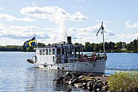 Domnarfvet är en ångdriven bogser- och varpbåt med en öppen för och en överbyggnad i aktern. Midskepps syns rök från skorstenen och i aktern svenska flaggan vajandes i vinden.