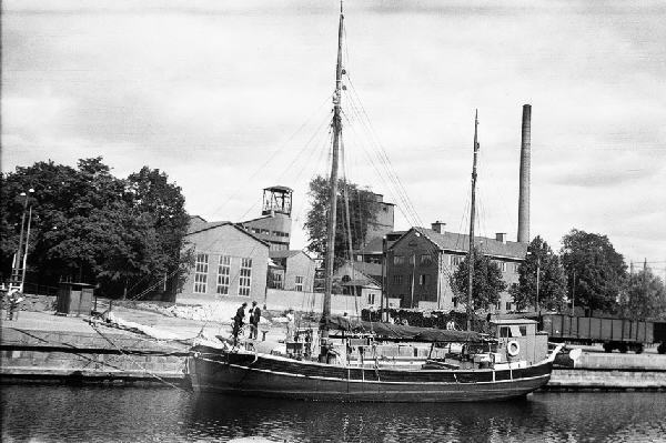 Emma är ett tvåmastat segelfartyg. Hon ligger förtöjd vid en kaj och seglen ligger i sina segelkapell längs bommarna. I aktern har hon styrhytten och i fören sticker ett bogspröt ut. Svartvitt foto från Uppsala hamn (Fyrisån). 