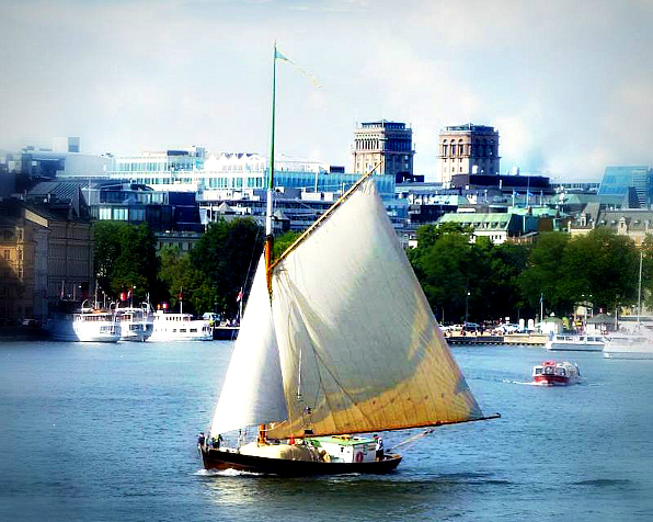 Helmi är en enmastad segelskuta med svart skrov och vita segel. På bilden syns fartyget på Nybroviken i centrala Stockholm. I bakgrunden syns Kungstornen.