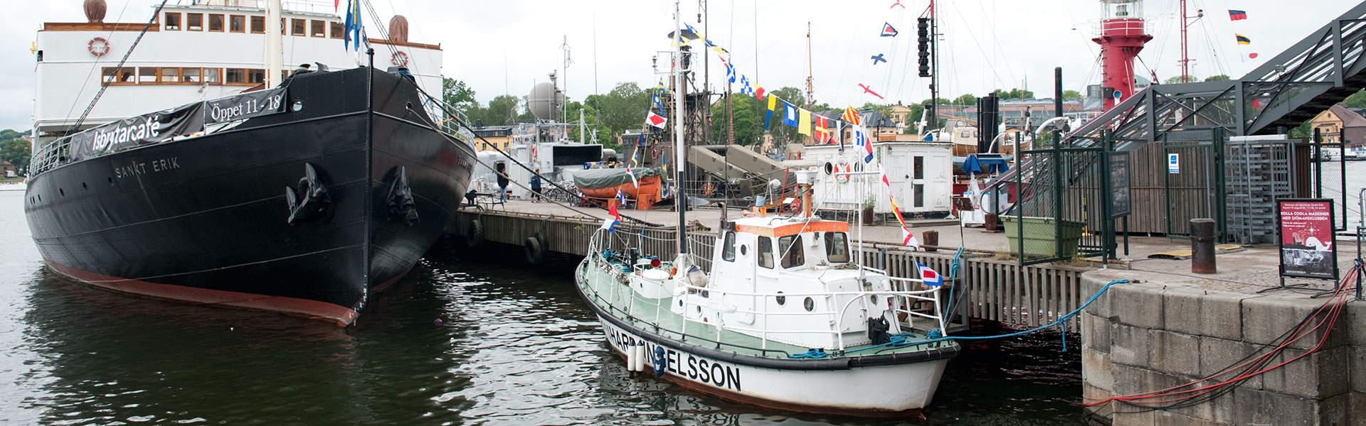 Isbrytaren Sankt Erik, stort ångfartyg med svart skrov och vit överbyggnad, ligger vid museifartygspriren. Sankt Erik ligger förtöjd långskepps med fören pekandes mot land. Förom Sankt Erik ligger ett mindre sjöräddningsfartyg. I bakgrunden syns museifartygspiren.