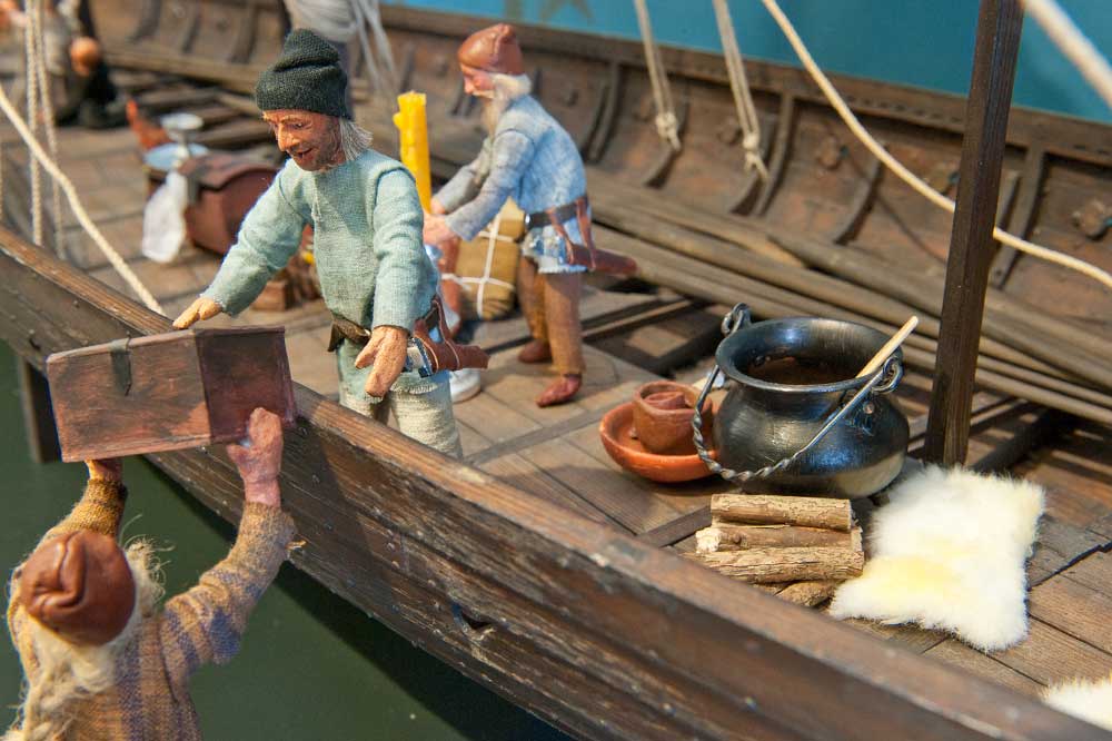 En skeppsmodell där miniatyrfigurer lastar varor.